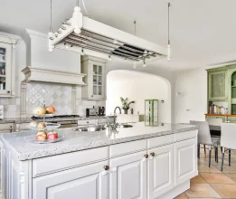 Traditional white kitchen with raised-panel island cabinetry, overhead hanging rack and open-plan dining area