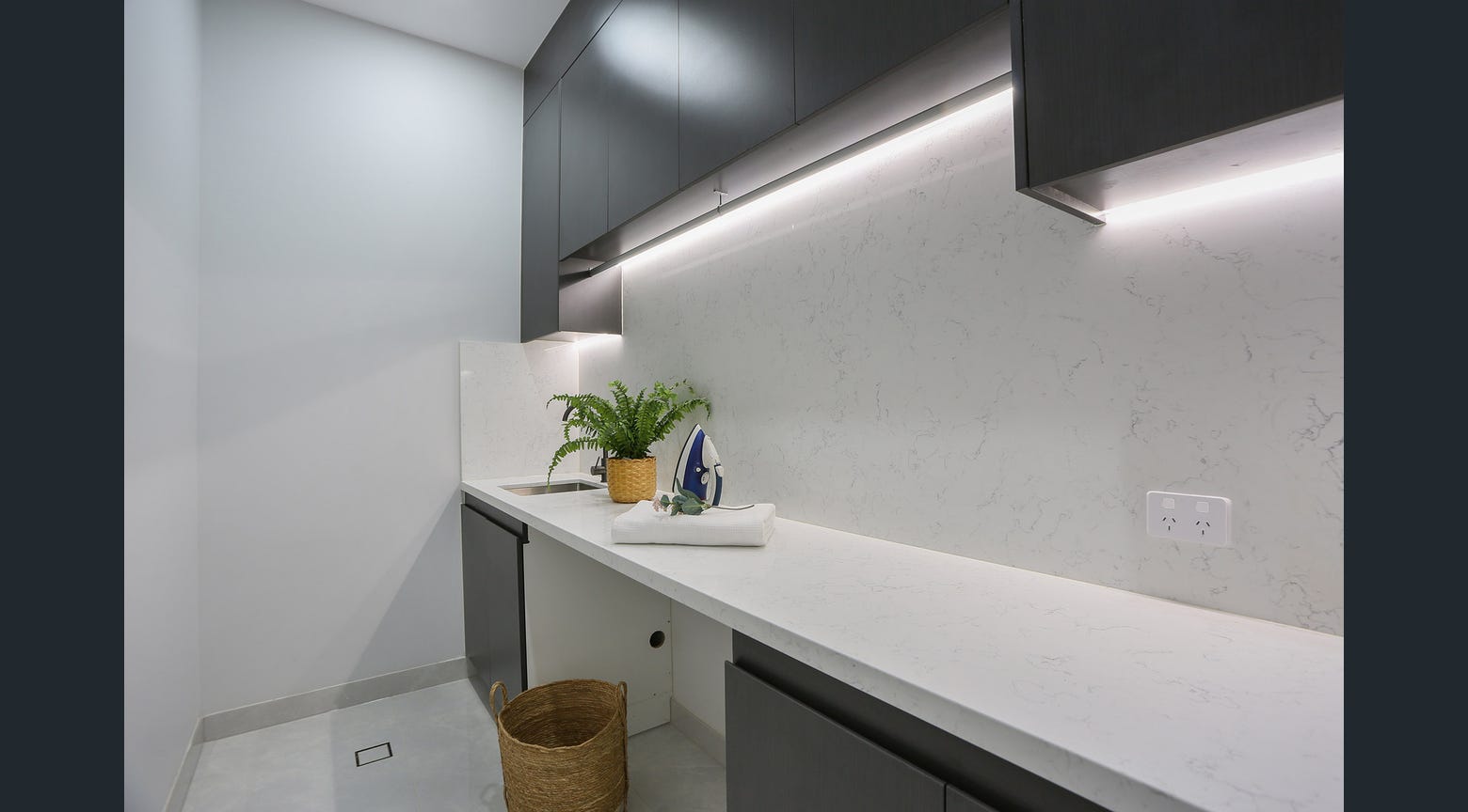Custom laundry cabinetry with dark upper cupboards, white stone benchtop and under-cabinet lighting
