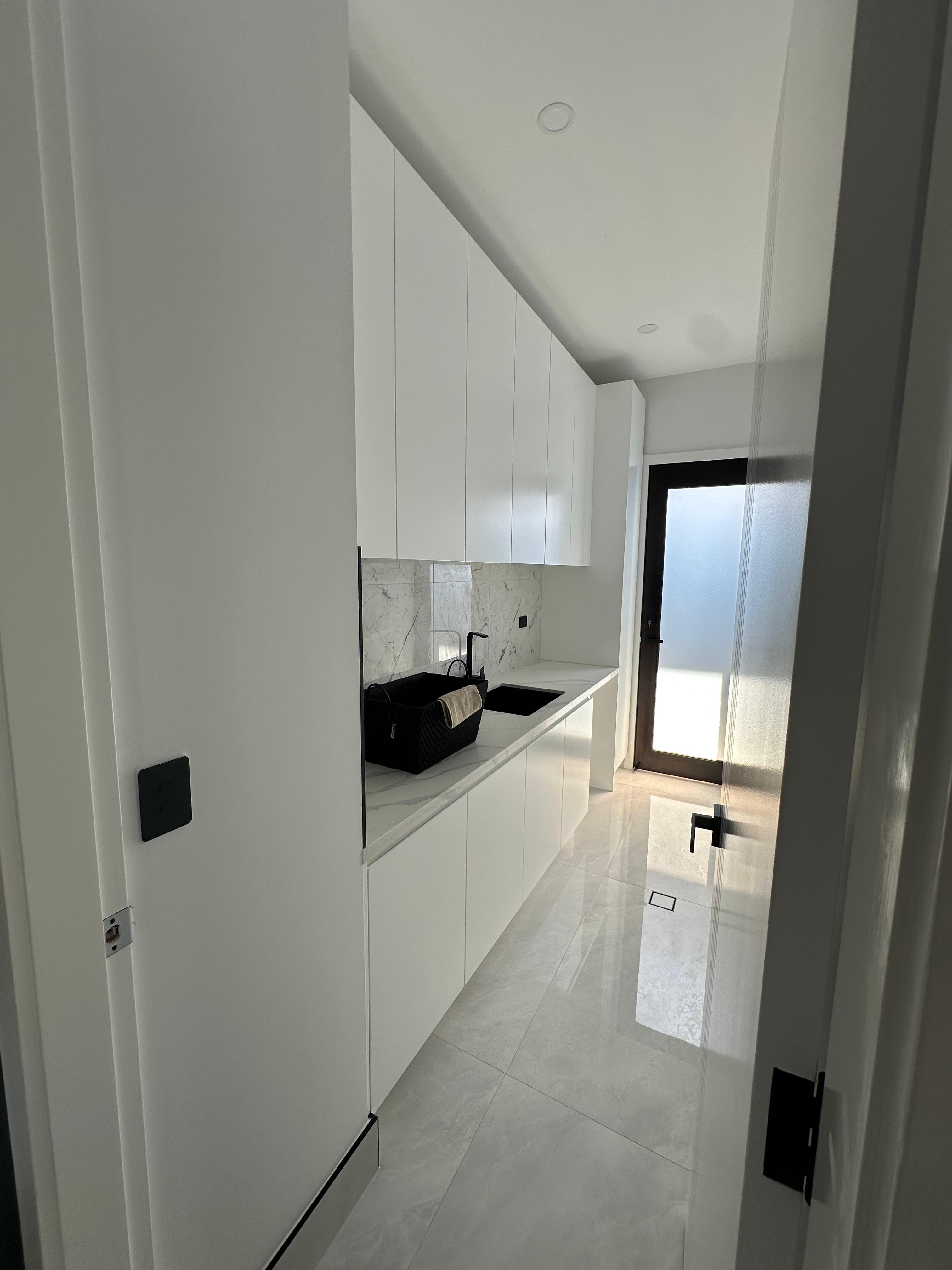 Compact modern laundry with white cabinetry, marble-look splashback, utility sink and frosted glass door