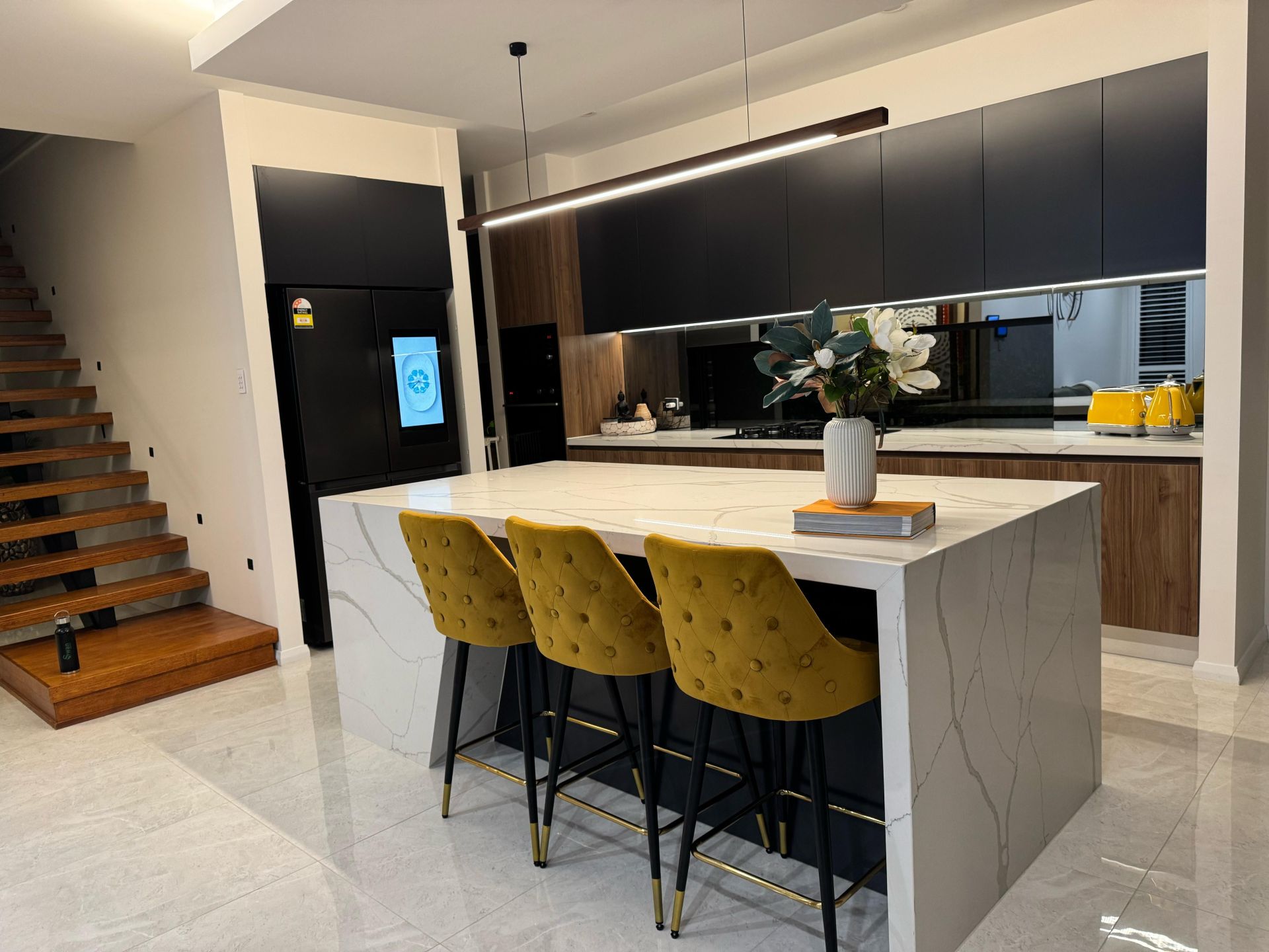 Modern kitchen with black cabinetry, wood accents, quartz island countertop and yellow bar stools