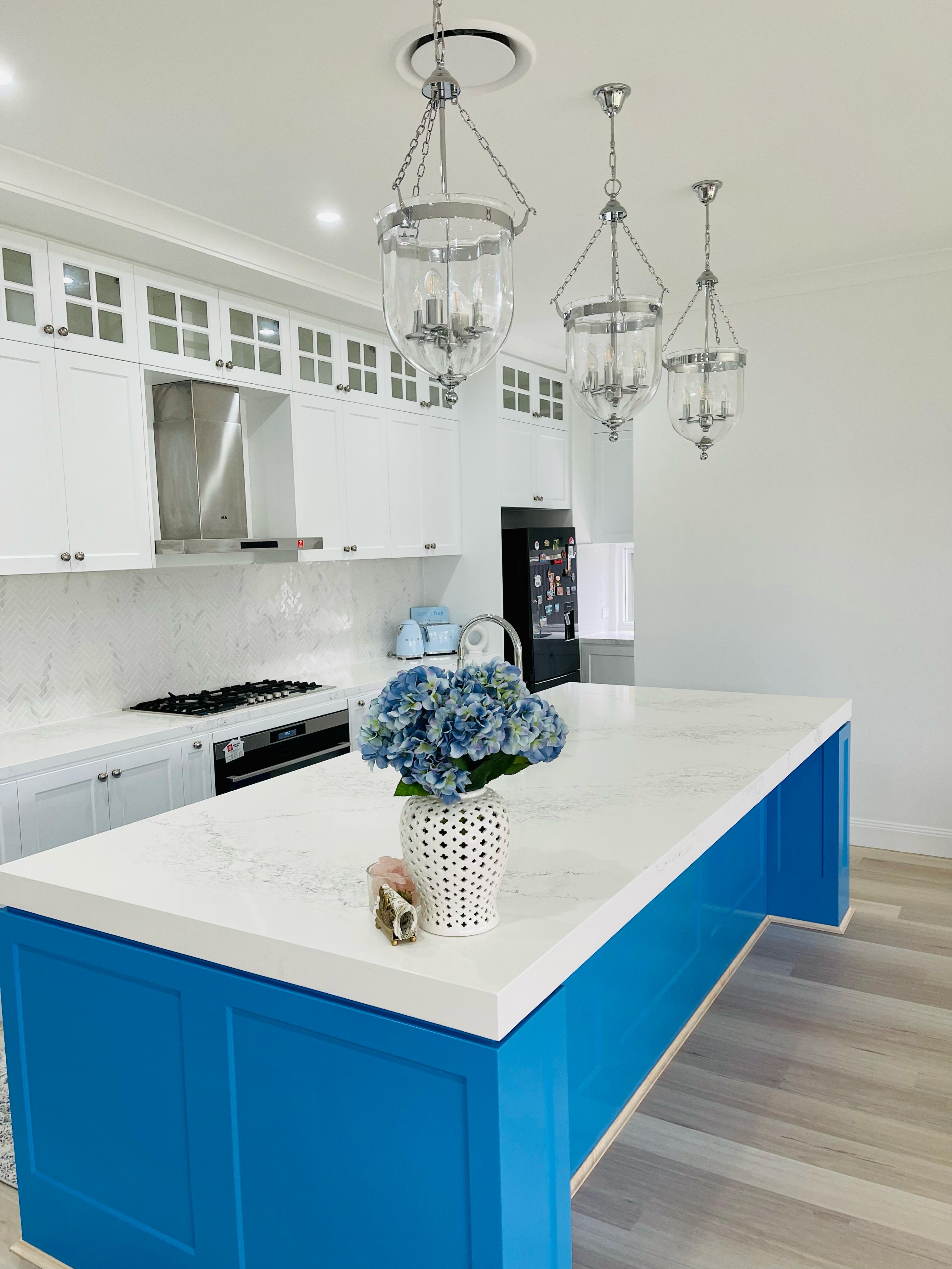 White kitchen with blue island cabinetry, quartz countertop, shaker cabinets and glass pendant lights
