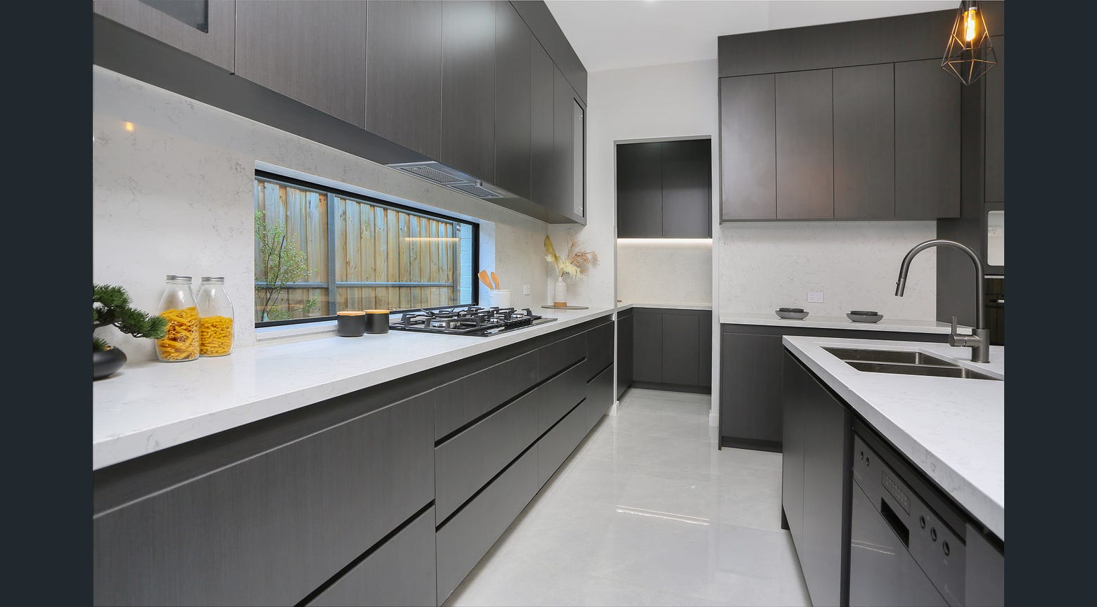 Dark custom kitchen cabinetry with white stone benchtops, gas cooktop and island sink