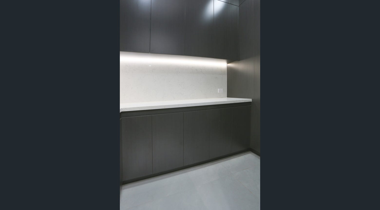 Minimalist dark kitchen cabinetry with white stone benchtop and integrated under-cabinet lighting