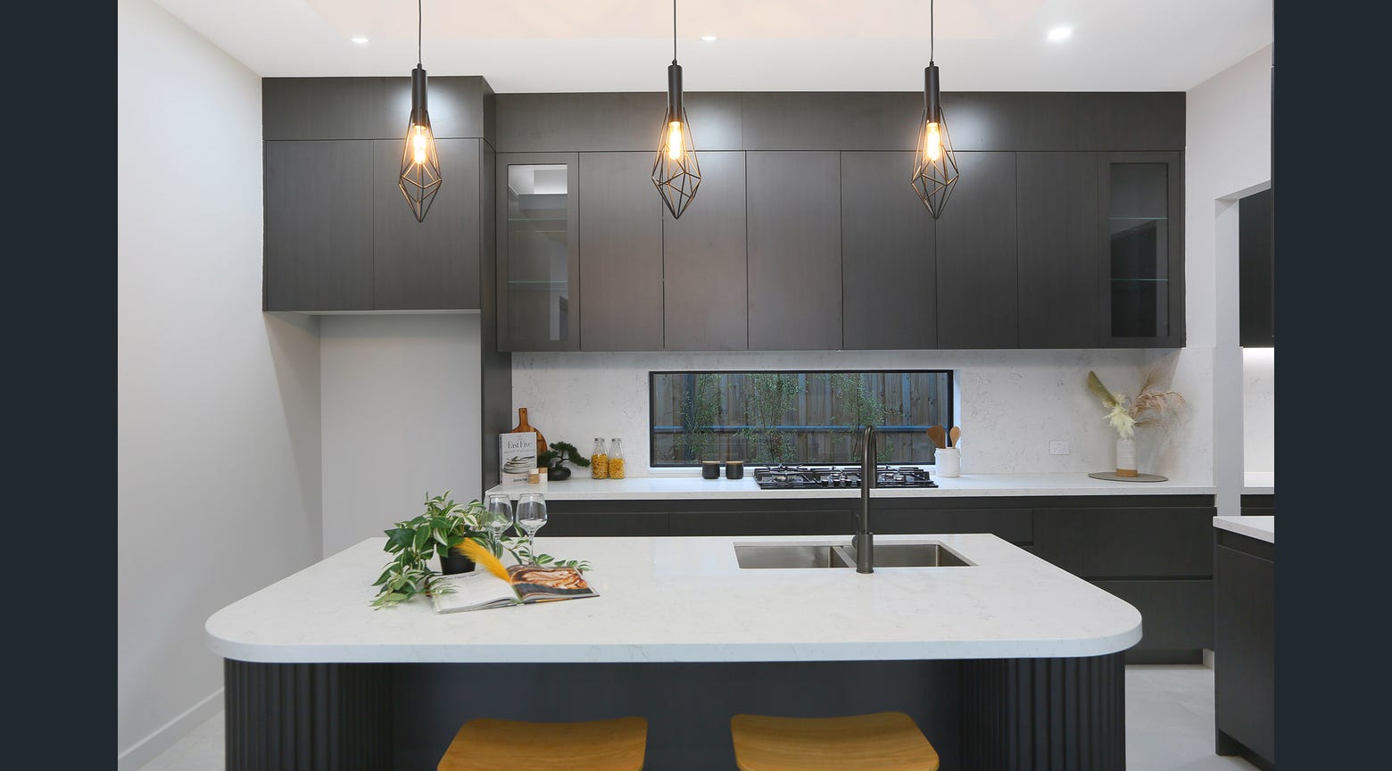 Custom dark kitchen with white stone island, integrated sink and pendant lighting