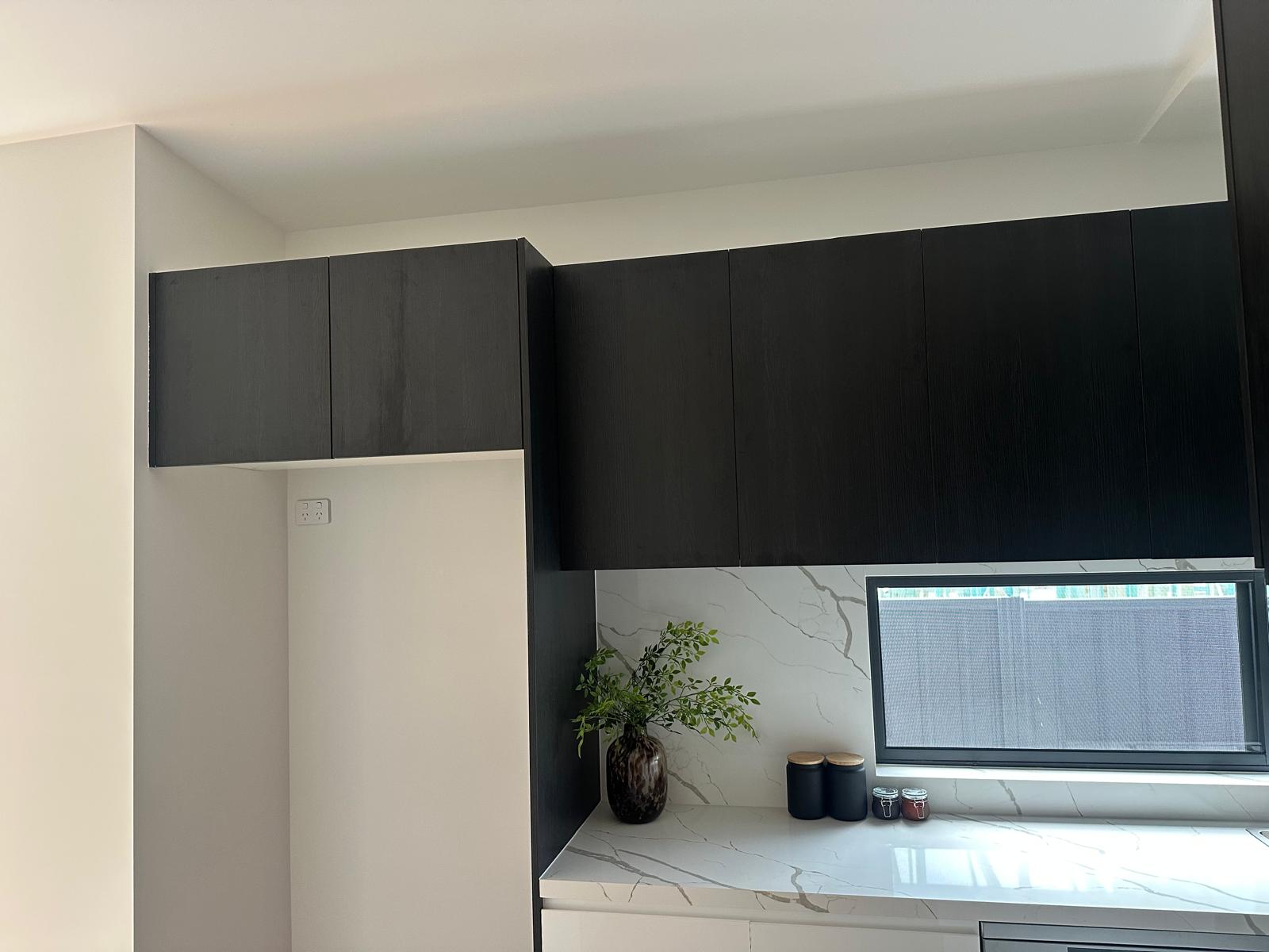 Black floor-to-ceiling kitchen cabinetry with marble-look benchtops and a horizontal window