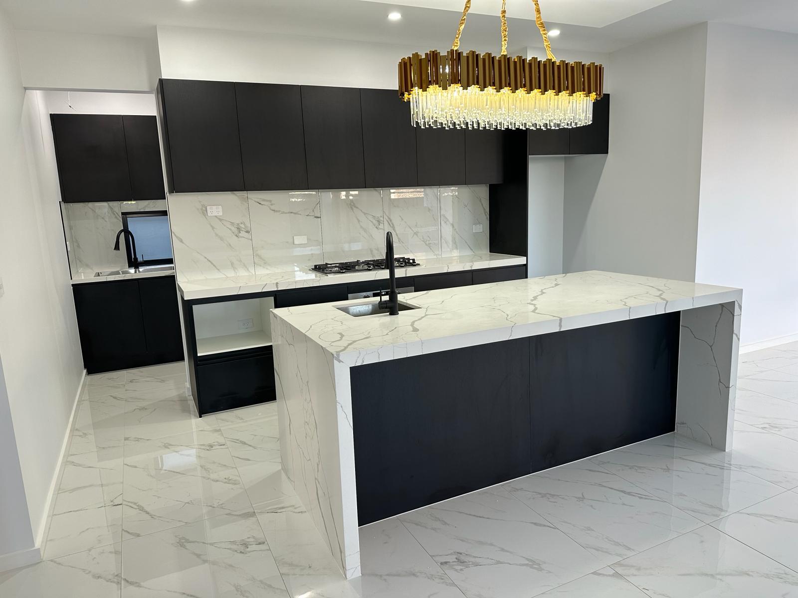 Luxury black and white kitchen with a marble-look waterfall island and pendant chandelier