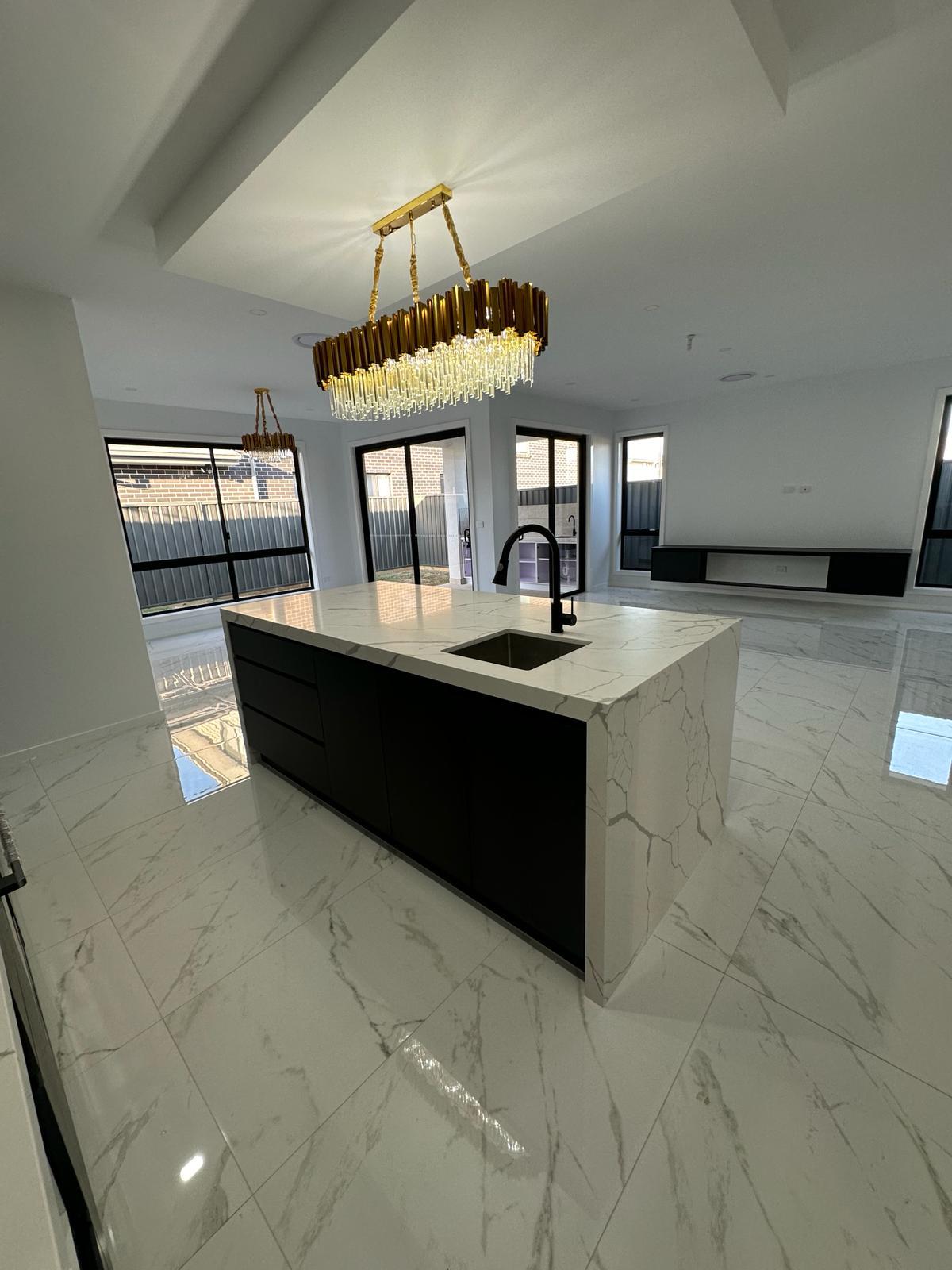 Custom kitchen island with black cabinetry, marble-look stone benchtop and integrated sink