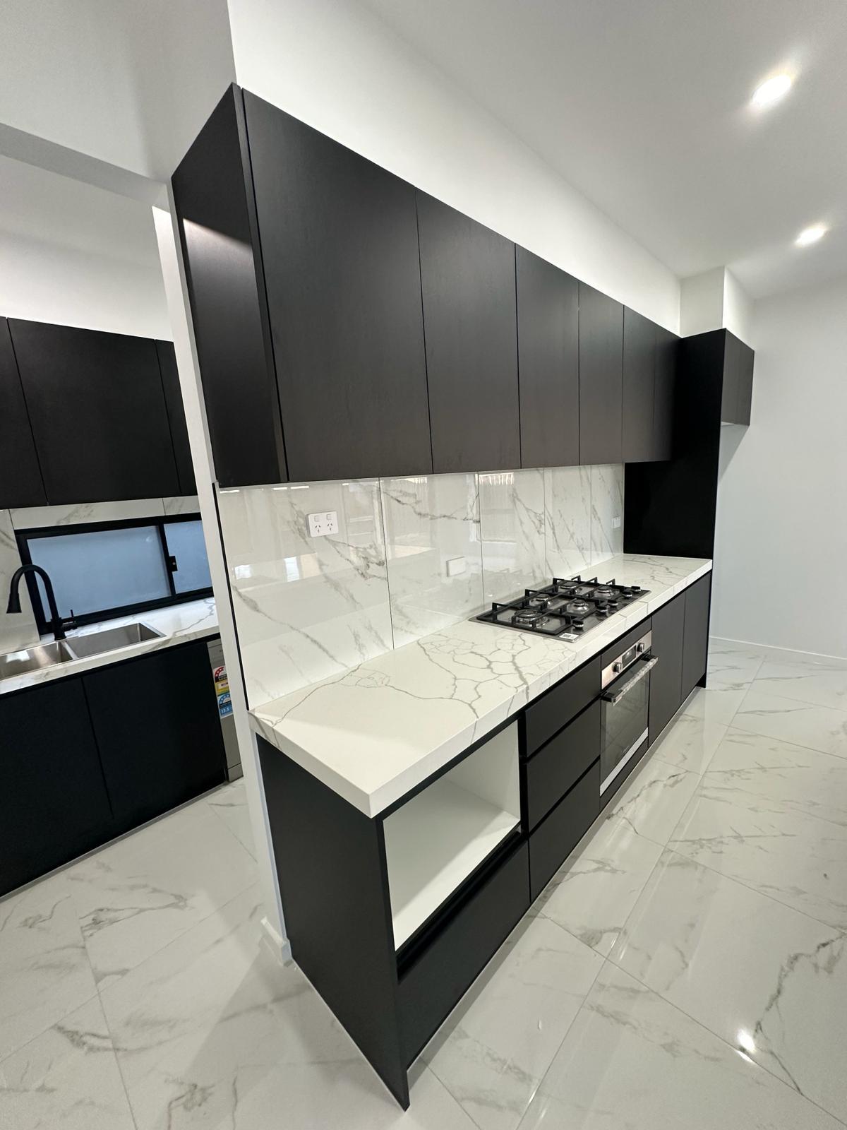 Modern black kitchen cabinetry with marble-look benchtop, gas cooktop and built-in oven