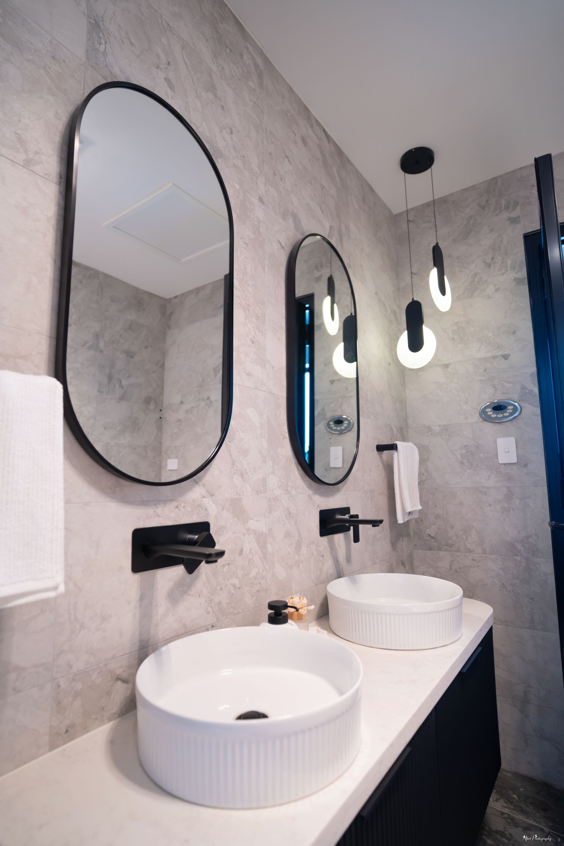 Custom bathroom vanity with white vessel basins, black tapware and arched mirrors