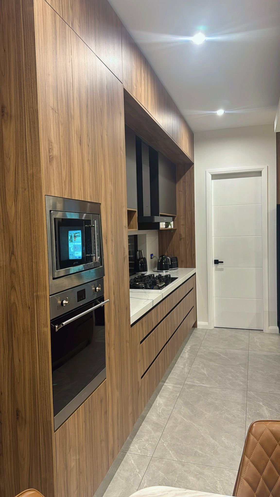 Modern kitchen with full-height timber cabinetry, built-in oven, gas cooktop and marble-look benchtop