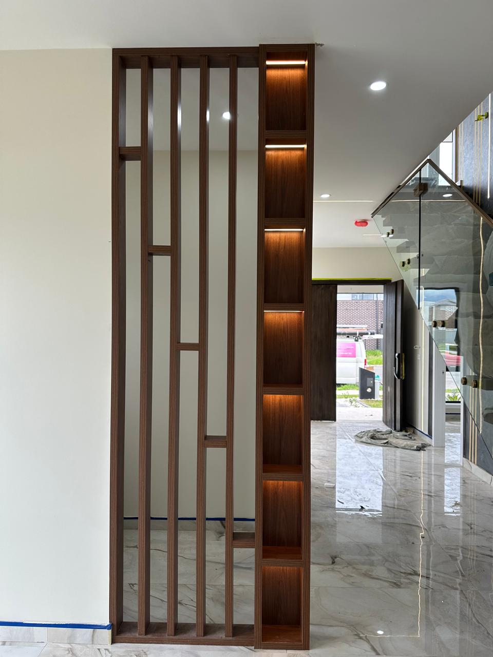 Custom timber slatted partition with warm LED-lit display shelving beside staircase