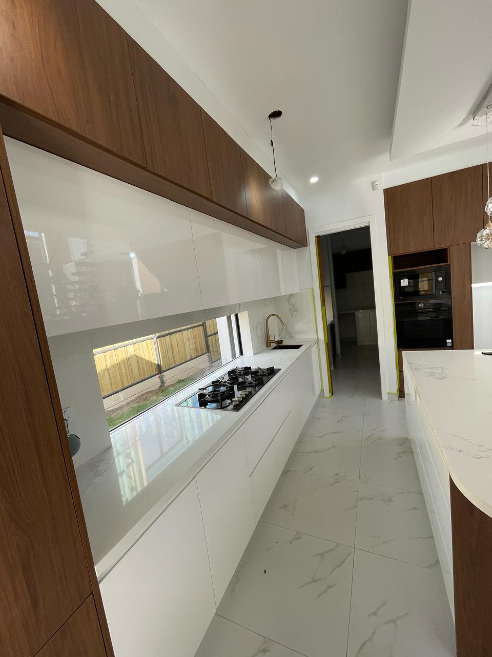 Modern kitchen with white lower cabinets, timber overhead cabinetry, gas cooktop, sink and large island