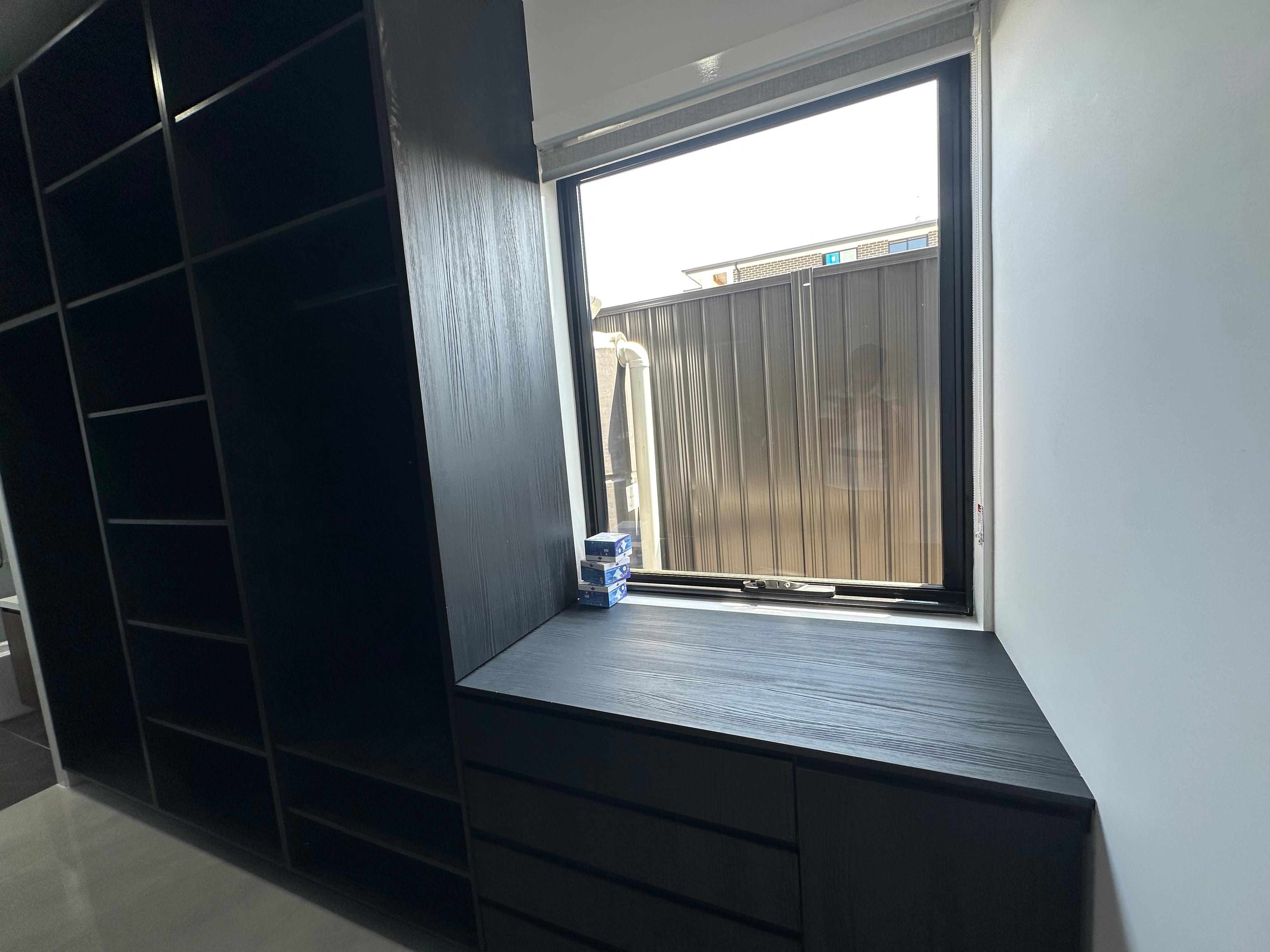 Custom black window seat with built-in drawers and surrounding wardrobe cabinetry