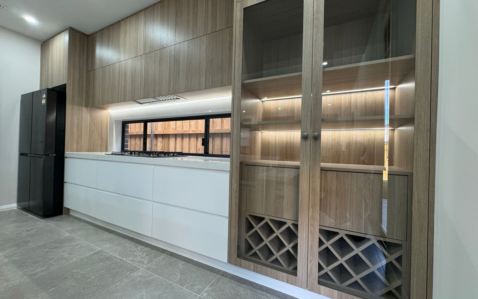 Modern kitchen with wood-grain cabinetry, white quartz island, black refrigerator and illuminated storage cabinets