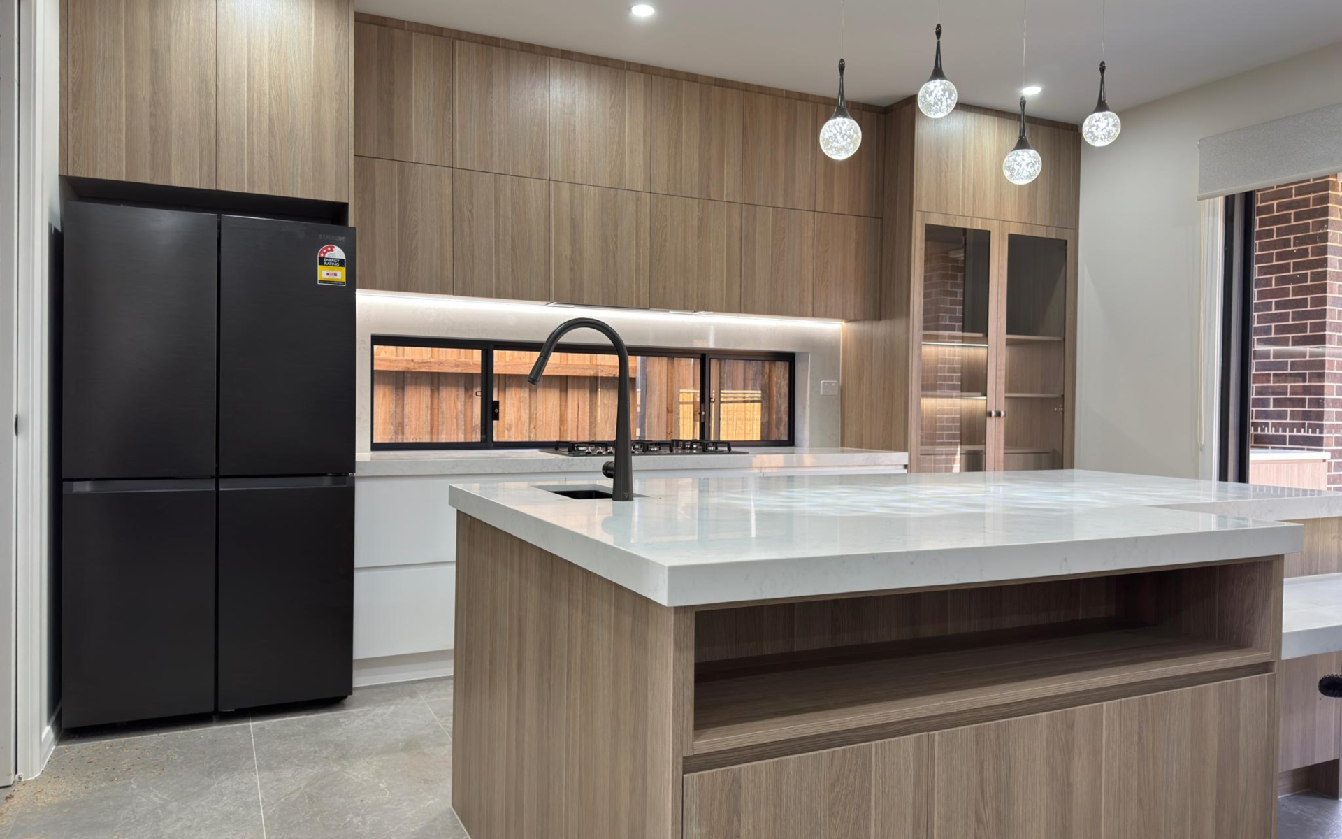 Wood-grain kitchen cabinetry with white quartz countertops, gas cooktop, built-in oven and window