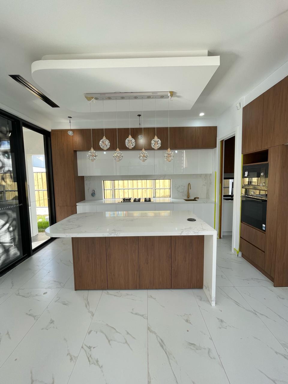 Modern kitchen with white and wood cabinetry, large quartz island, black appliances and decorative lighting