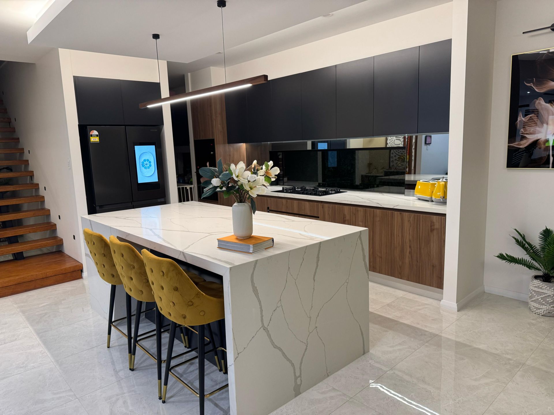 Modern kitchen with black upper cabinets, wood cabinetry, large quartz island and yellow bar stools