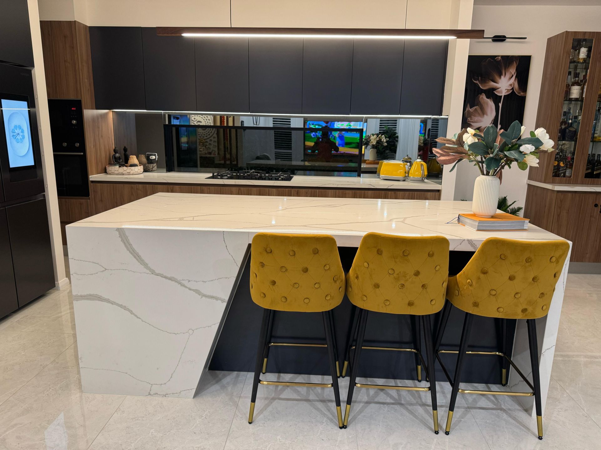 Contemporary kitchen with black cabinetry, wood accents, quartz island and mirrored backsplash