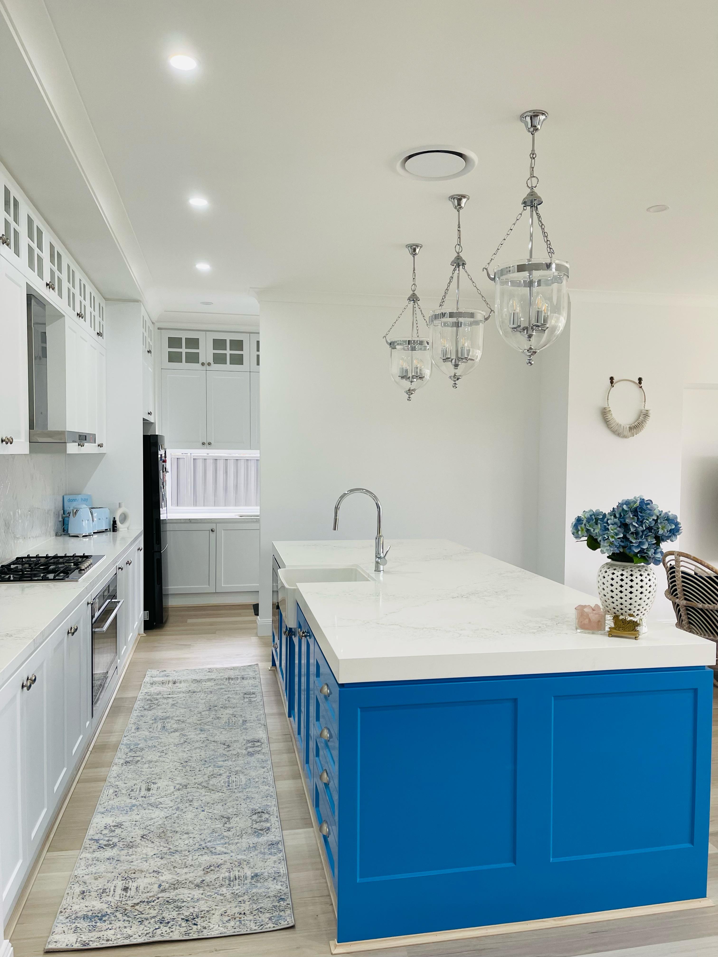 Bright kitchen featuring blue island cabinets, white shaker cabinetry, quartz countertops and decorative pendant lighting