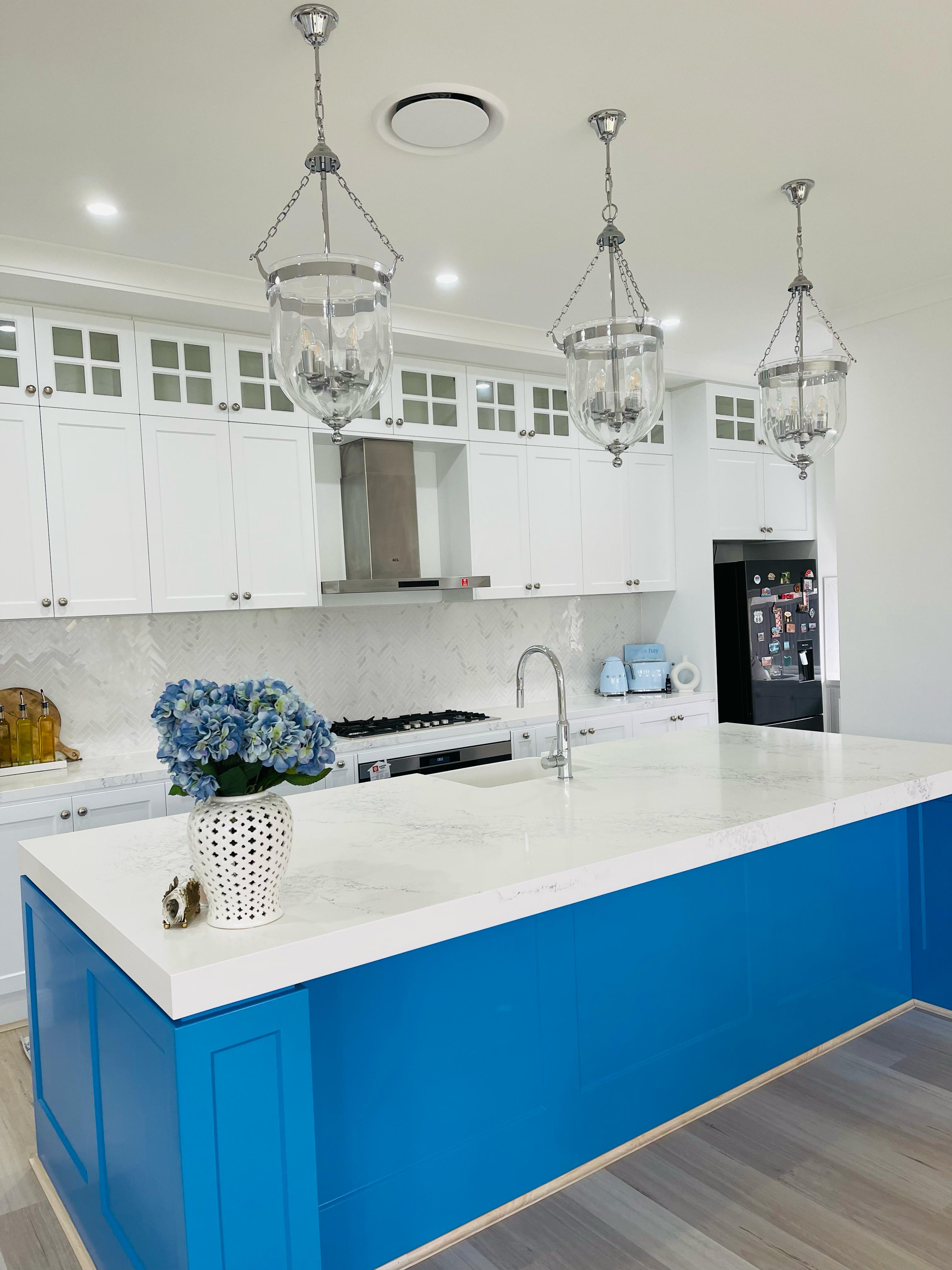 Modern white kitchen with shaker cabinets, quartz countertop, herringbone backsplash, gas cooktop and range hood