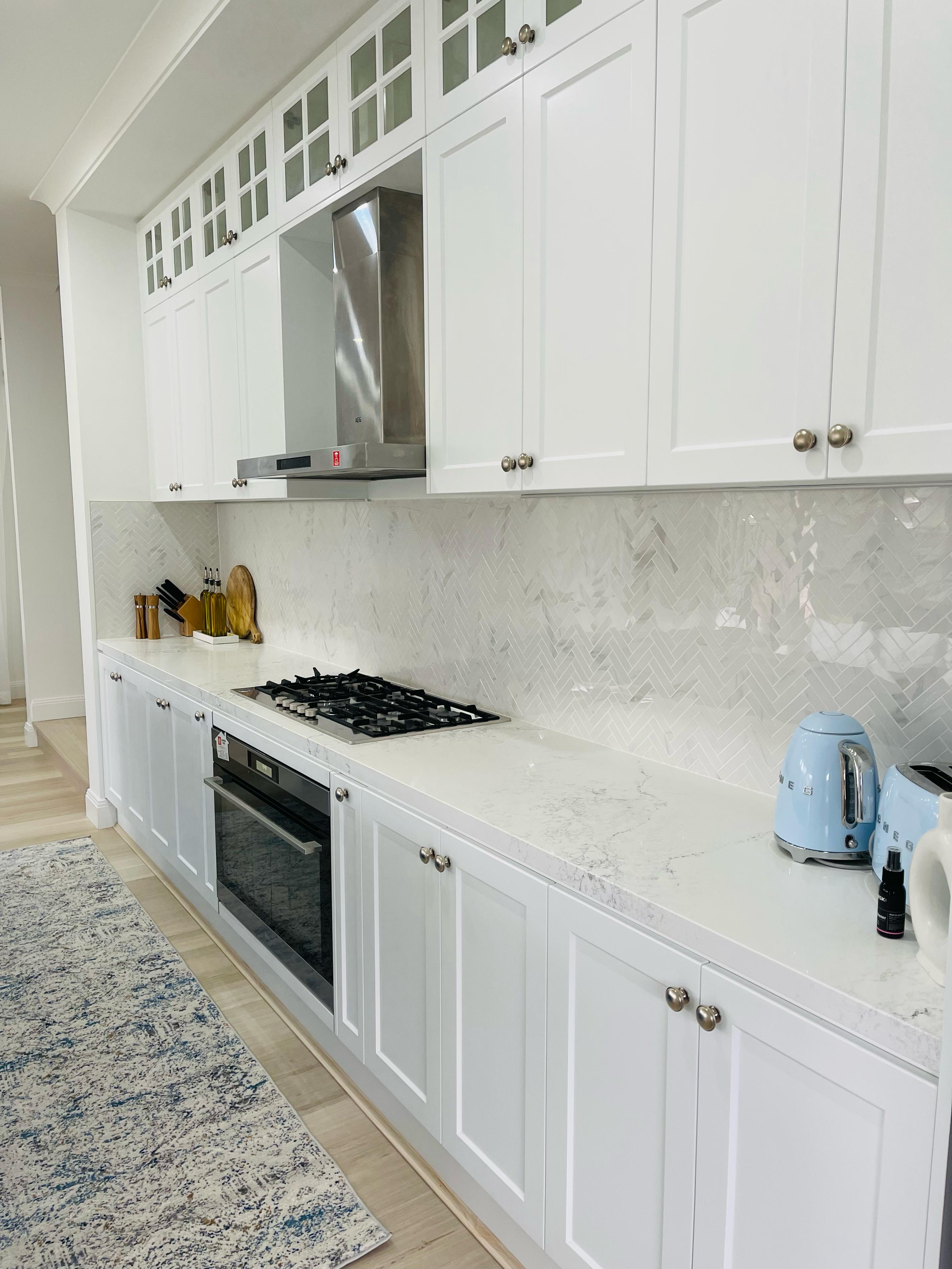 White shaker kitchen with quartz countertops, herringbone backsplash, gas cooktop and stainless steel range hood