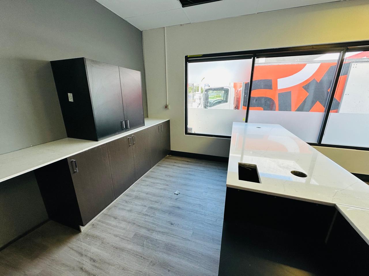 Custom office kitchenette featuring dark storage cabinets, white benchtops and large windows