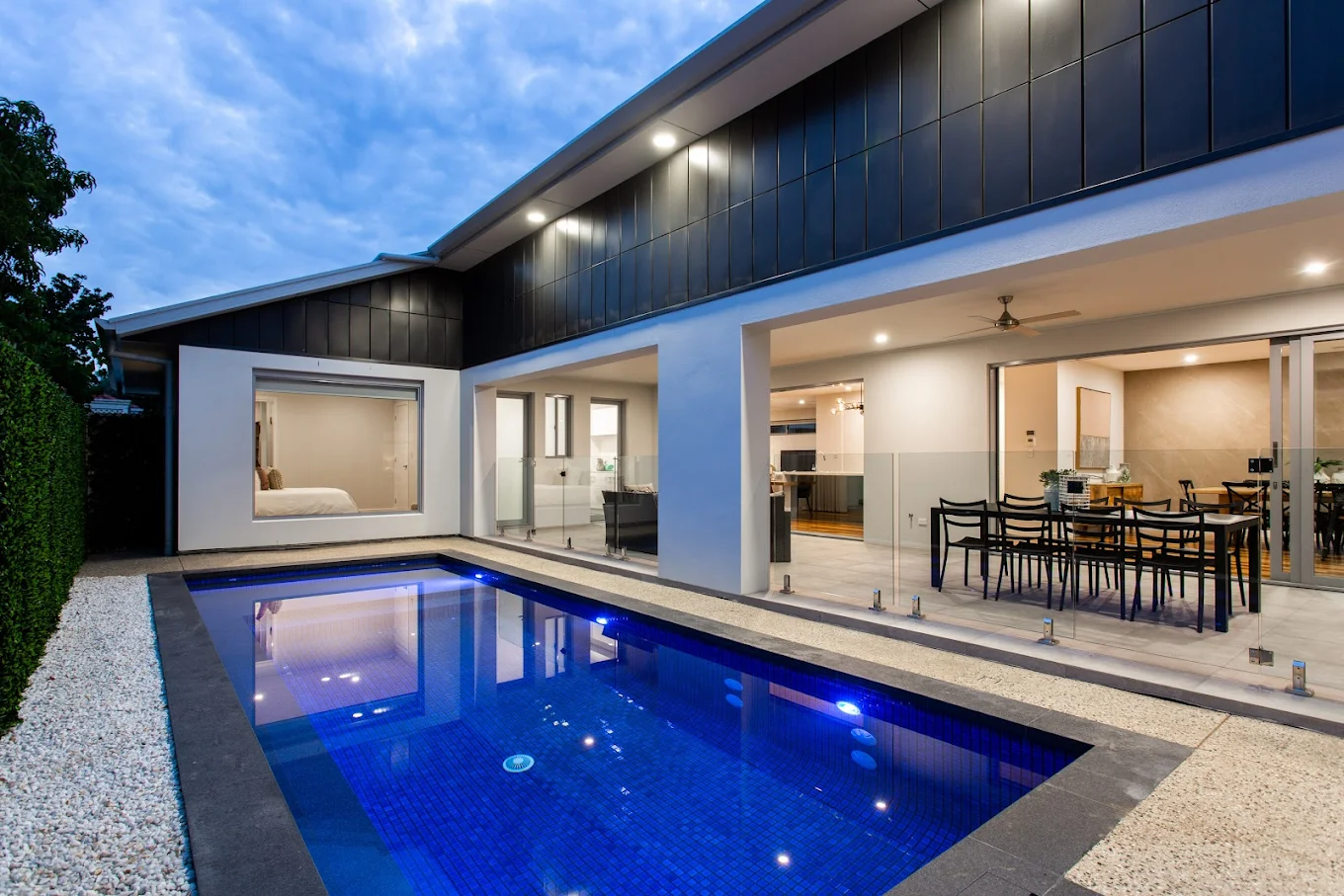 Modern home with custom outdoor entertaining area overlooking an illuminated swimming pool