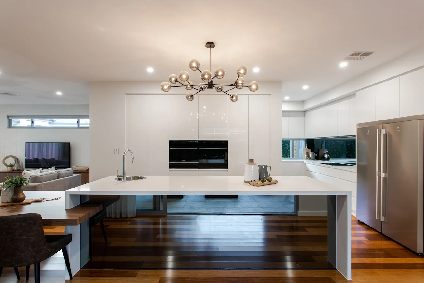 Custom white kitchen cabinetry with large island bench, integrated appliances and timber flooring