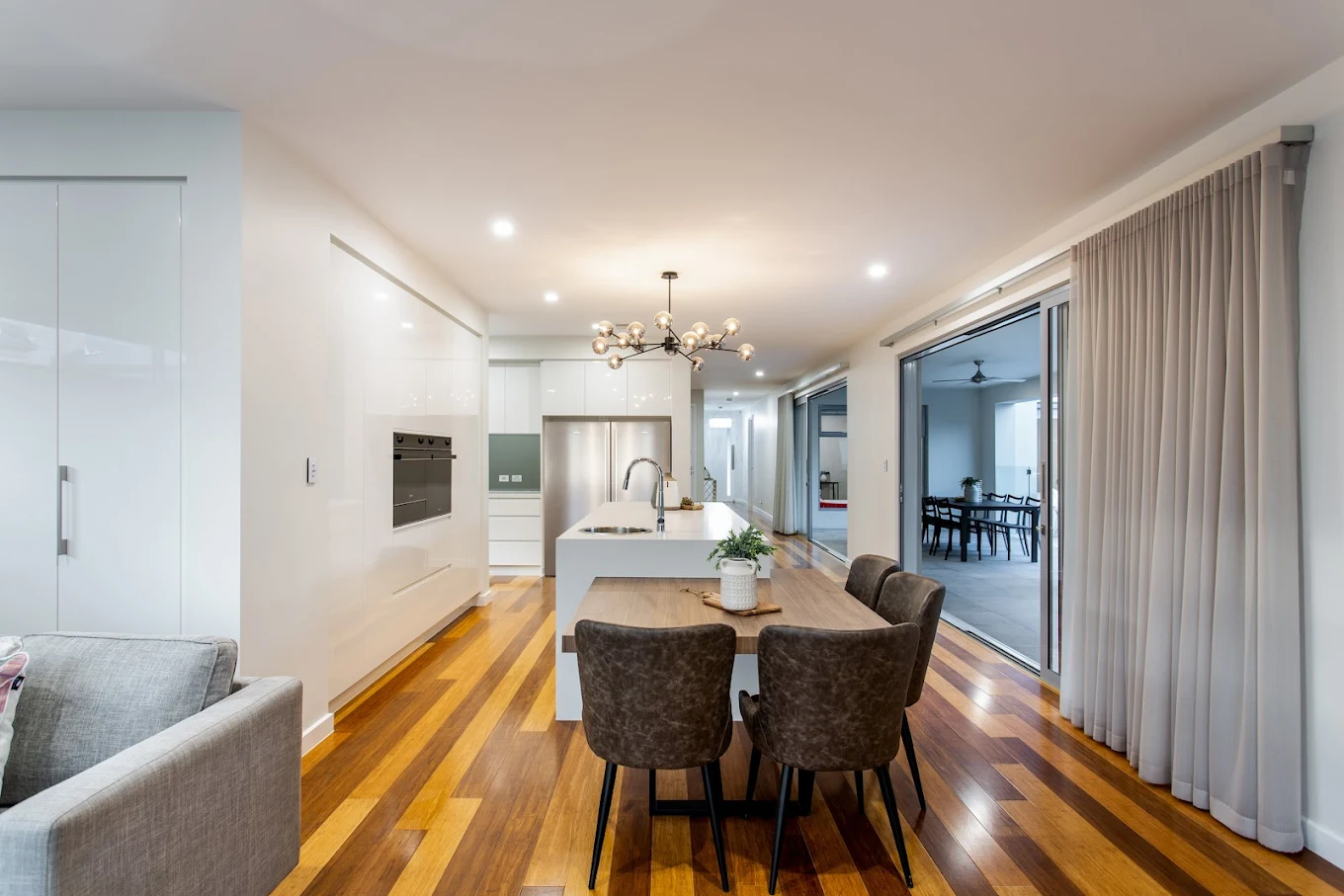Open-plan custom kitchen with white cabinetry, island bench, timber dining table and polished timber flooring
