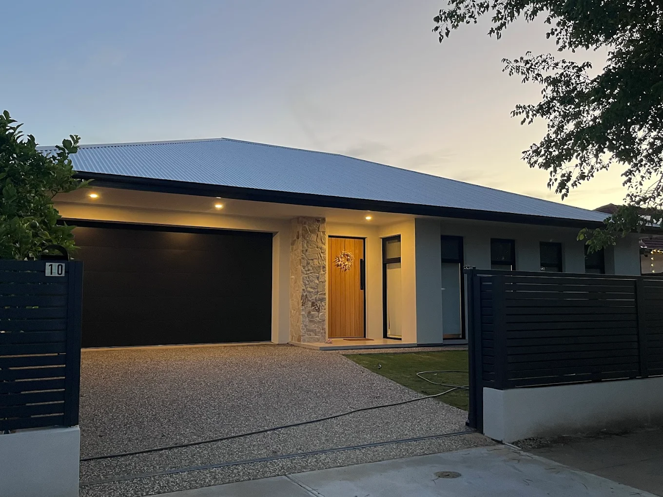 Modern single-storey home exterior at dusk with timber front door, stone feature wall and black fence